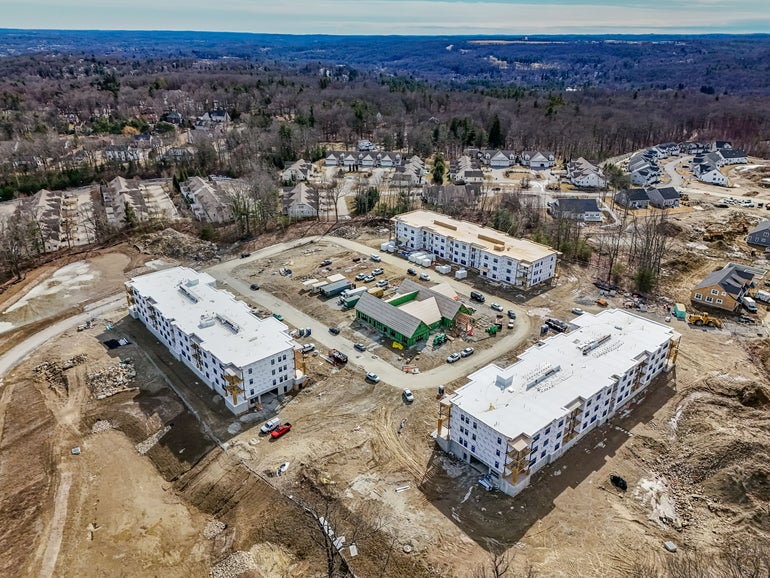 An aerial shot of a three-building apartment compelx being constructed on a hill top.