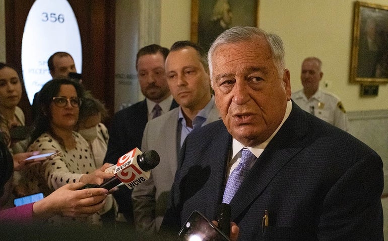 A man in a dark suit is interviewed by reporters.