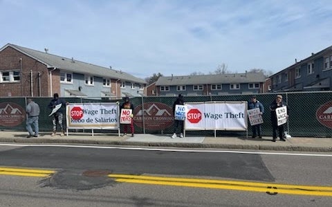 Demonstrators hold signs outside of a construction site.