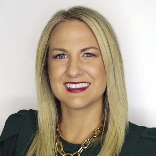 A woman with blonde hair wears a green shirt and a gold chain.