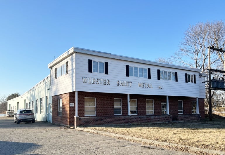 A photo of a red brick a white sided industrial building with metallic lettering reading 