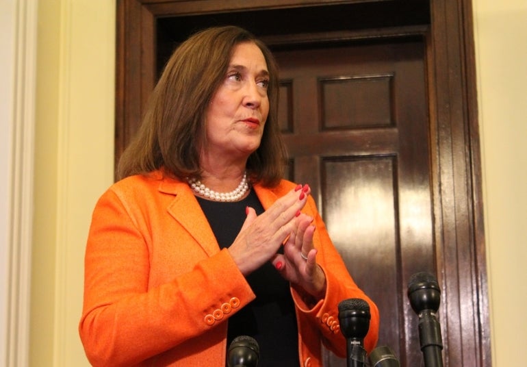 Woman in orange suit speaks at microphones