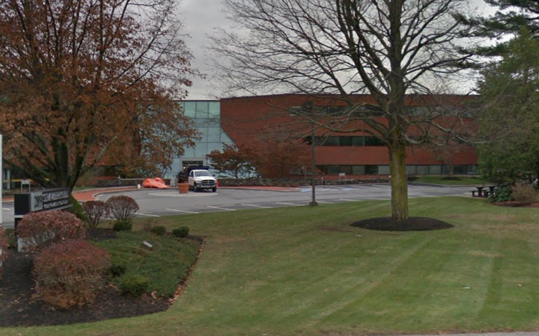 a three-story brick office building sits in front of a parking lot and small lawn.