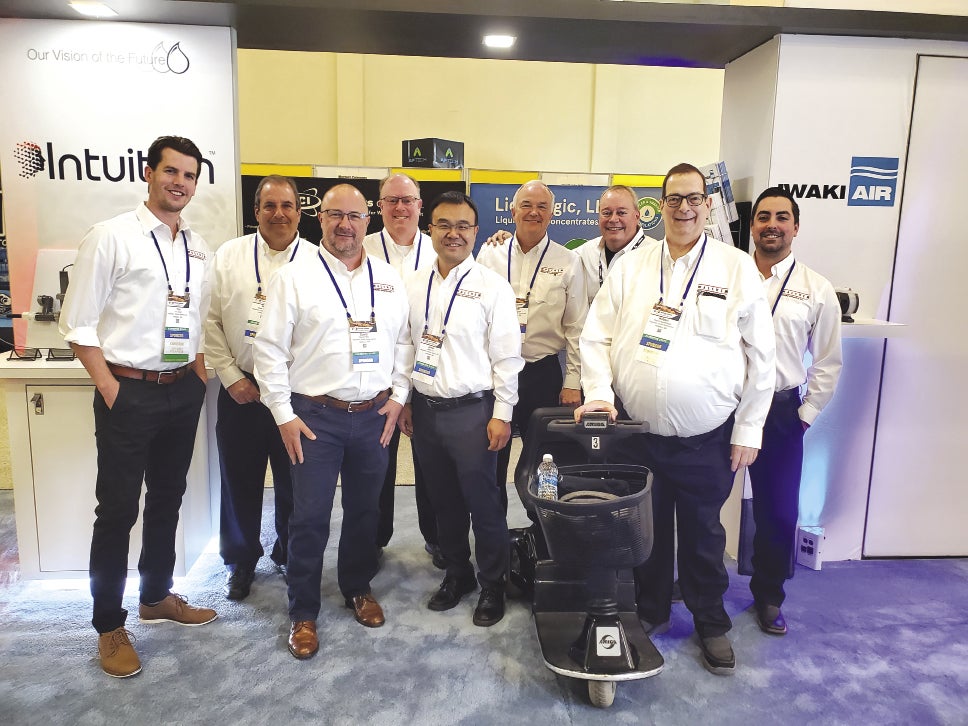 A group of nine men wearing white button down shirts and lanyards stand beside each other.
