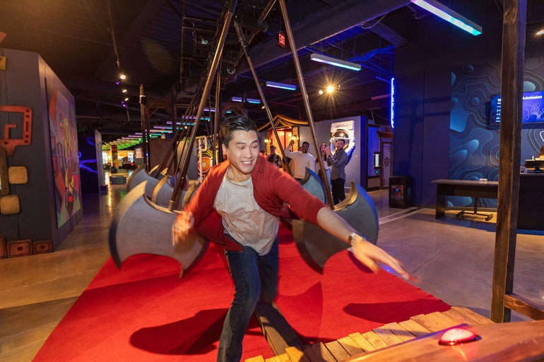 Person running through an obstacle course made of foam axes, reaching to press a red button at the end of the course.