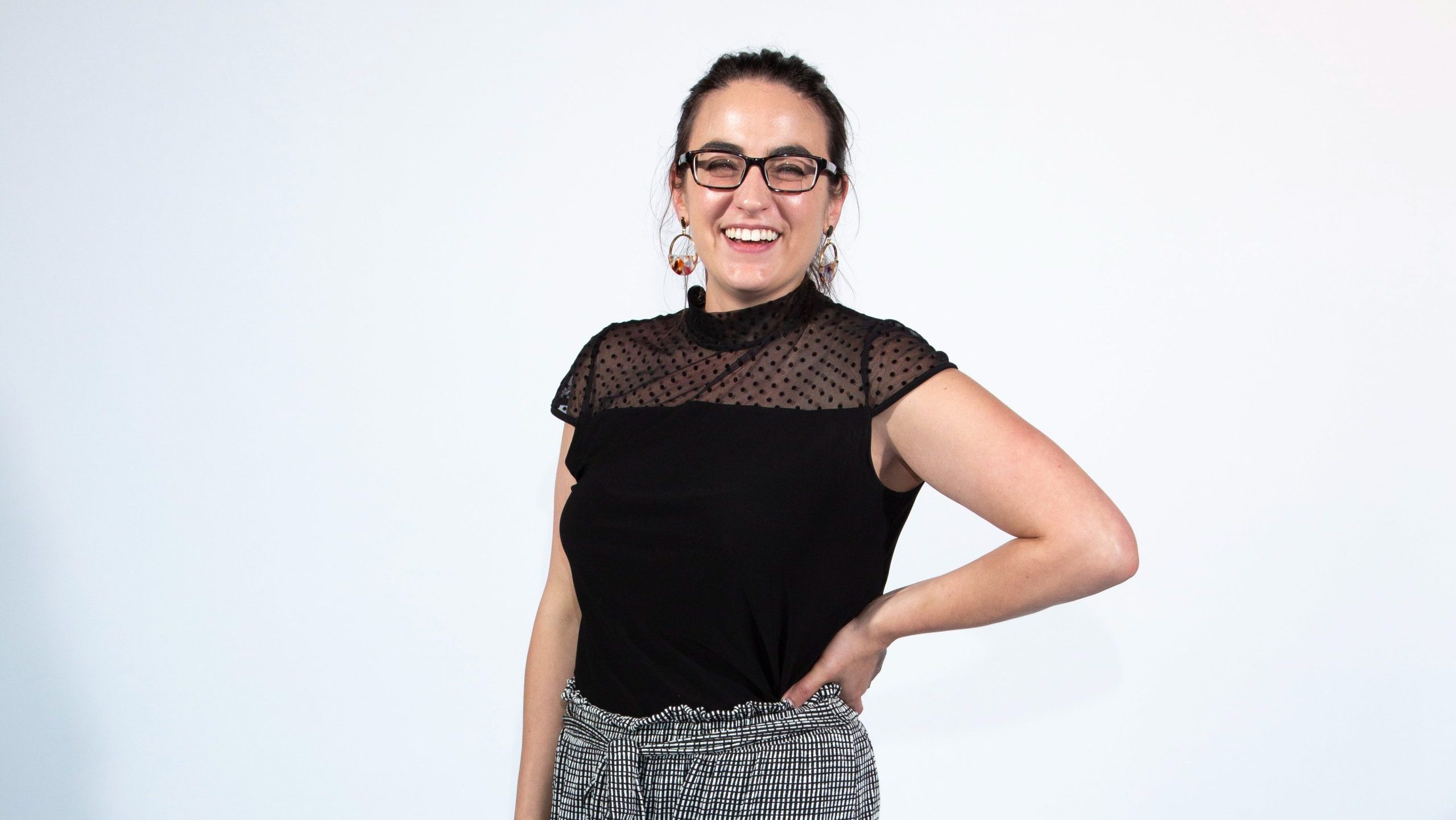 A woman in a black shirt smiles with a hand on one hip