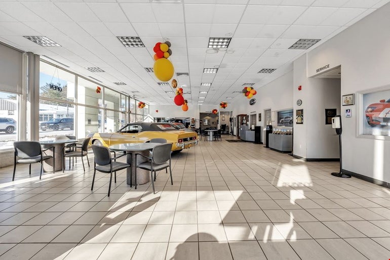 A car dealership with tables and chairs in foreground and an antique muscle car behind.