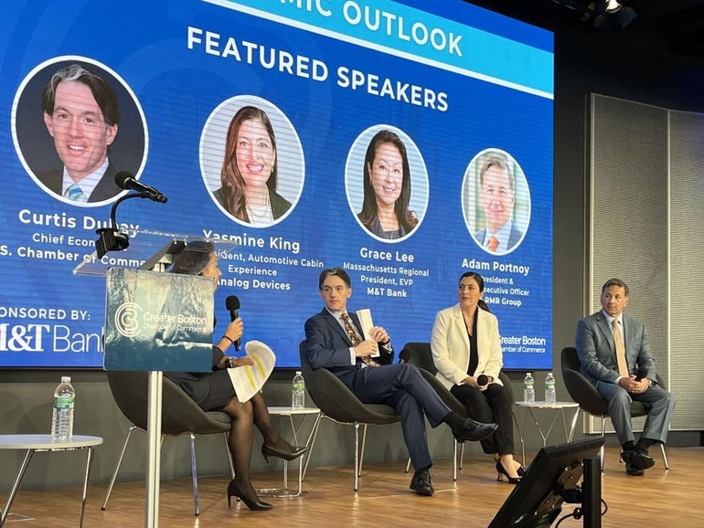 four people sitting on a stage talking with a blue background behind