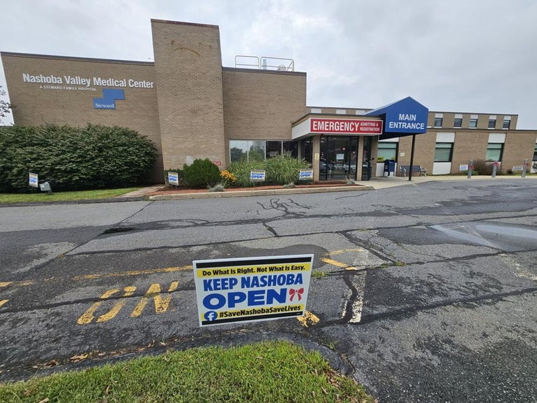 A brick emergency room sits behind a large driveway with a sign on it reading 