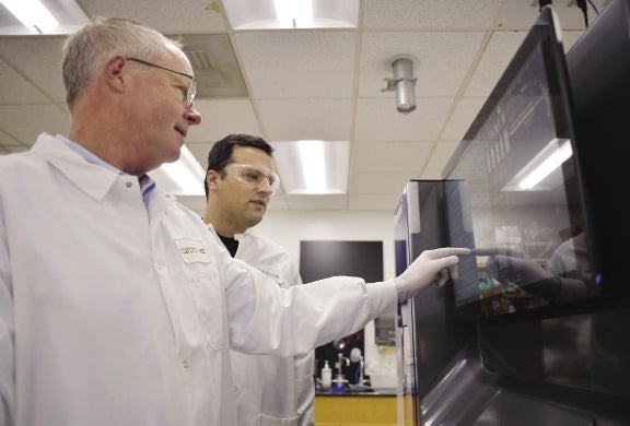 Stine stands with a fellow Abbvie researchers and points to something not visible displayed on a screen.