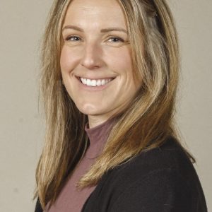 A woman with blond hair is wearing a black jacket and purple sweater.