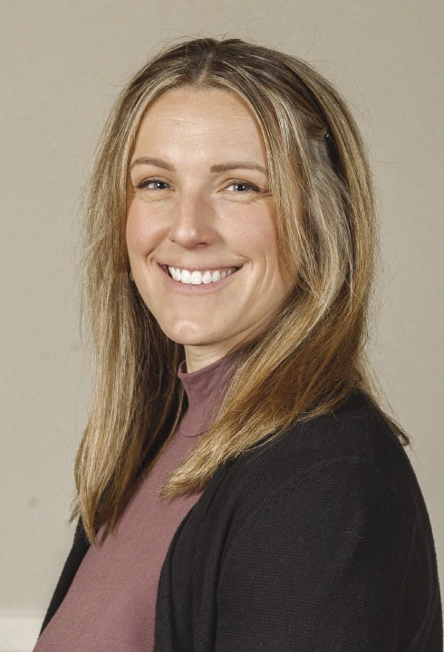A woman with blond hair is wearing a black jacket and purple sweater.