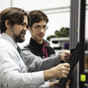 Two Multiscale Systems employees are pictured in a workshop looking at a black composite.