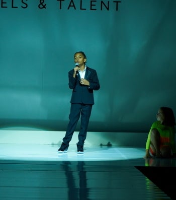 A young man in a suit speaks into a microphone on a stage