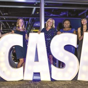 Five women standing behind large letter cutouts that spell C-A-S-A