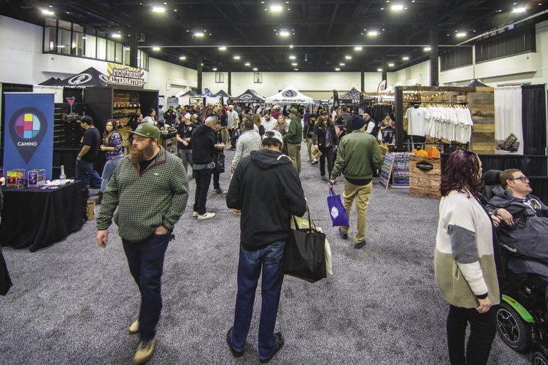 Many people walking around a expo floor, with booths set up on the right and left.