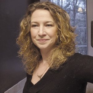 A woman with blonde wavy hair wears a black top.
