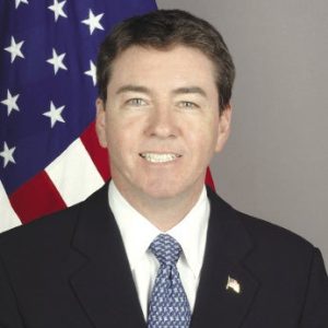 Man in suit stands in front of American flag