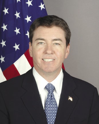 Man in suit stands in front of American flag