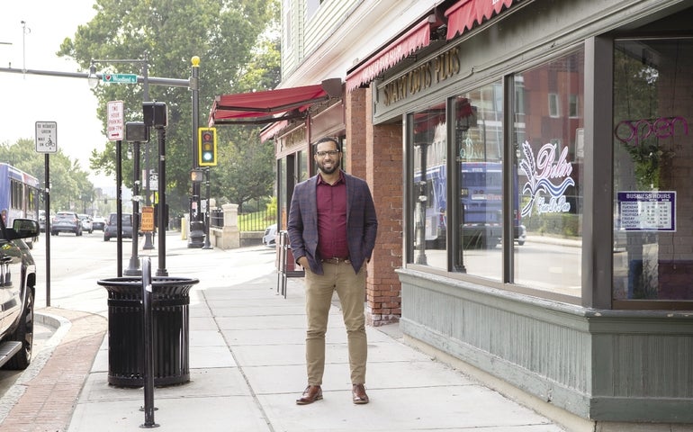 A man with a beard and glasses stands smiling in front of a barber shop