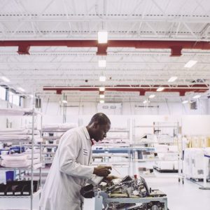 A man in a lab coat cleans a piece of machinery in an industrial building