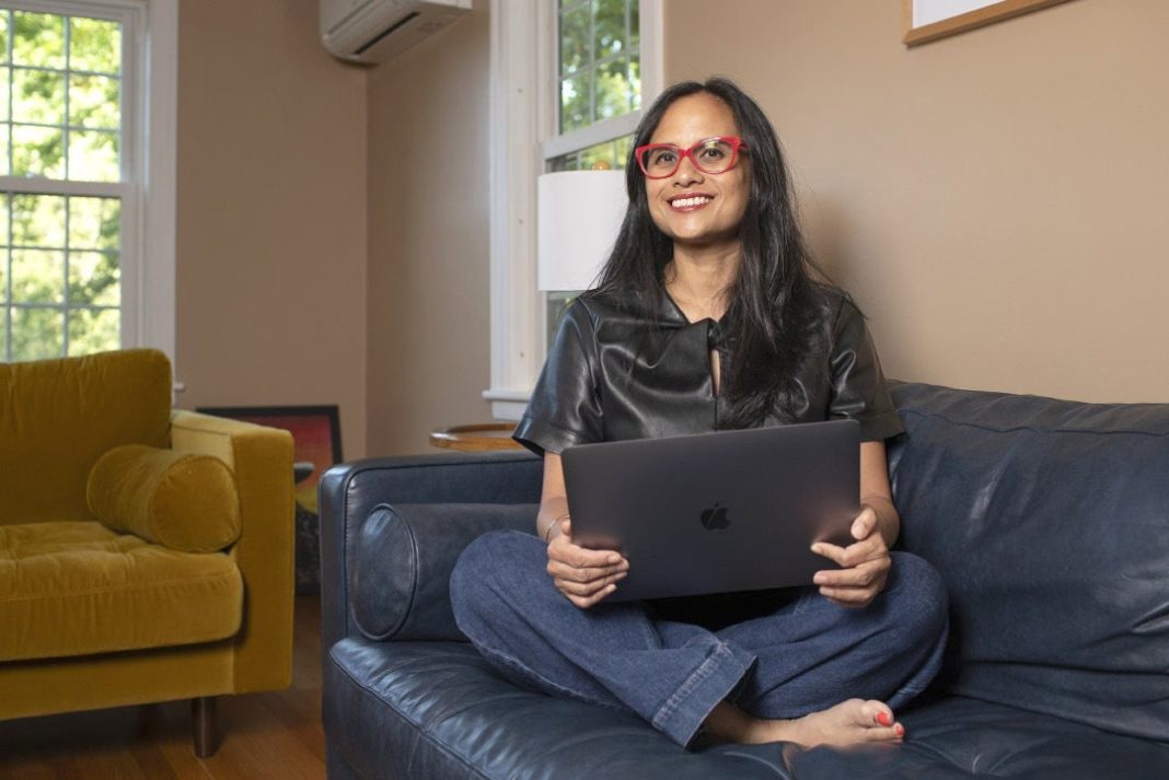 A woman sits with a computer on a couch