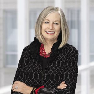 A woman with a grey bob wears a black patterned sweater.