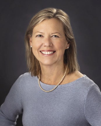A woman with shoulder-length blonde hair wears a pearl necklace and light blue top.