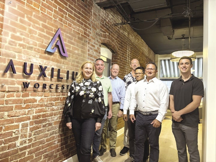 Seven people stand inside a hallway next to a brick wall with a sign reading 