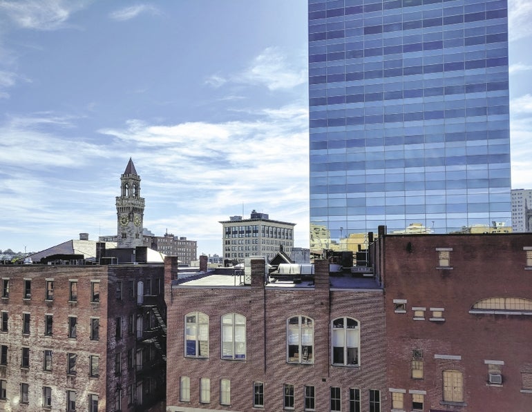 Worcester's skyline, with smaller brick facade buildings in front of a glass skyscraper and City Hall's clock tower.