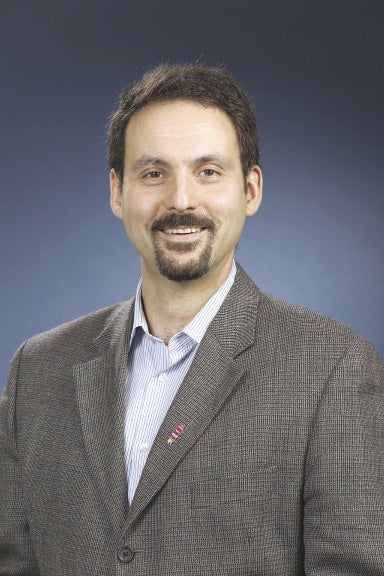 A man in a suit jacket stands in front of a blue background