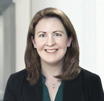 A woman with brown hair wears a black jacket and dark green blouse.