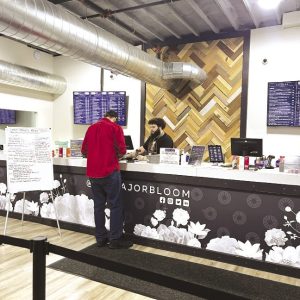 A customer and a cashier stand at a retail counter inside a cannabis dispensary.