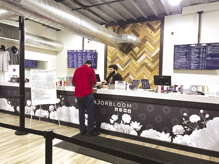 A customer and a cashier stand at a retail counter inside a cannabis dispensary.