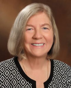 A woman with chin-length grey hair wears a black and white patterned top.