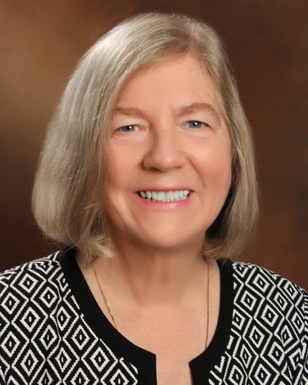A woman with chin-length grey hair wears a black and white patterned top.