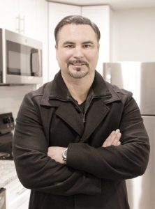 Man stands in black coat with arms crossed