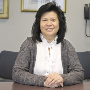 A woman sits at her desk with her hands folded in front of her.