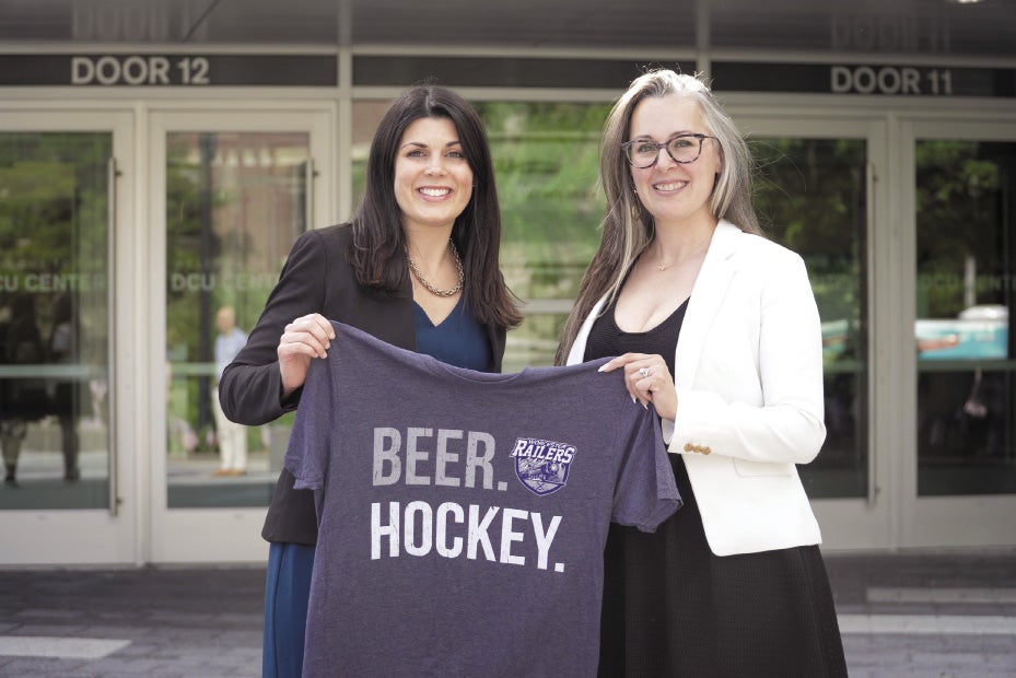 Two women stand in front of the DCU Center holding a jersey that says 