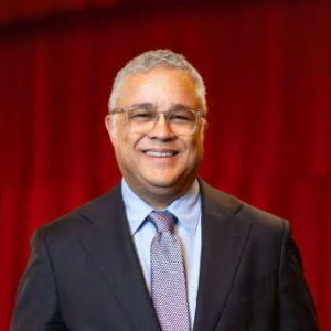 Man stands in suit in front of red curtain