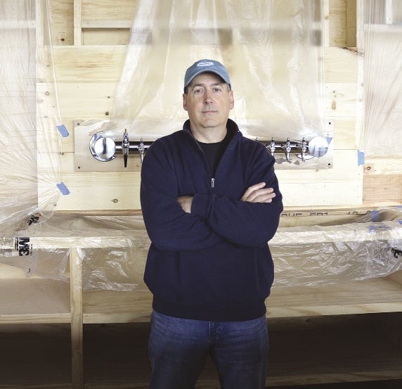 Will Oliveira stands with his arms crossed in front of a bar in mid-construction.