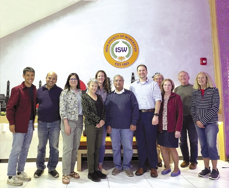 Eleven people stand together under a sign reading 