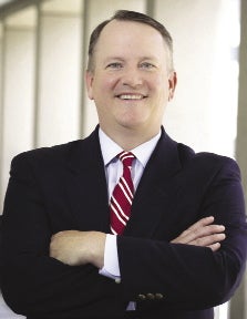A man in a black suit and red and white striped tie with crossed arms