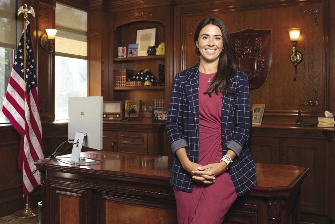 A woman sits on a wooden desk with a wood panel background
