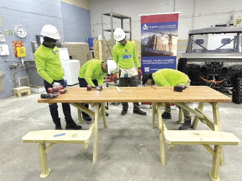 Four workers construct a picnic table inside a shop