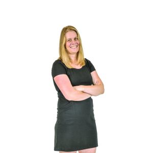 A woman in a black dress smiles with arms folded