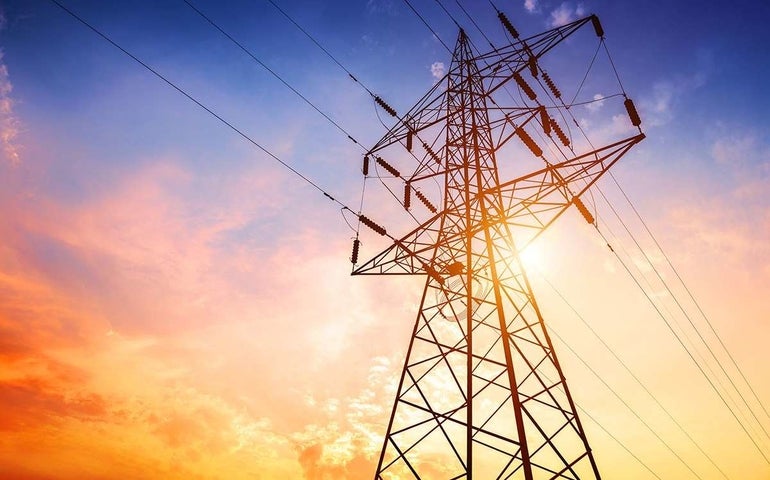 An electricity transmission tower set against the setting sun