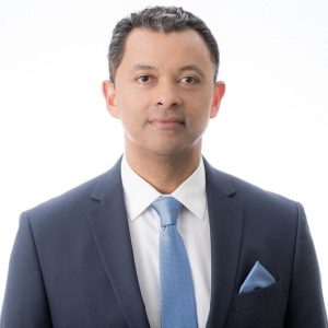A man in a blue suit with a white button down and light blue tie.