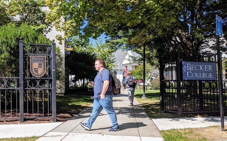 A male student with a backpack walks in front of a black iron gate