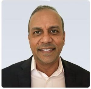 A man with short hair wears a black blazer and white button down.